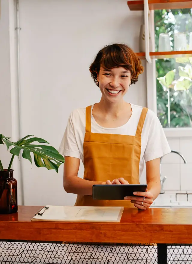 Una emprendedora sonríe detrás del mostrador de su tienda con una tablet