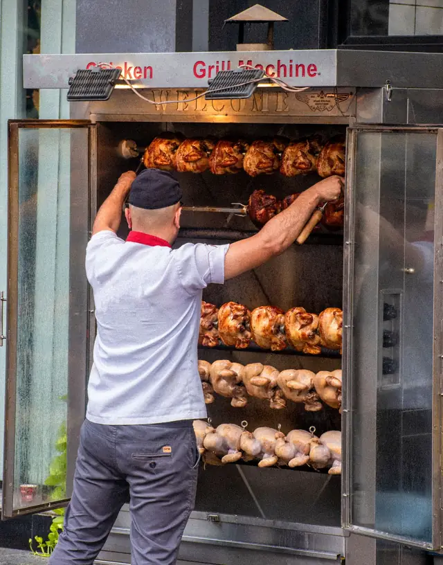 Un cocinero prepara pollos a la brasa en la rosticería